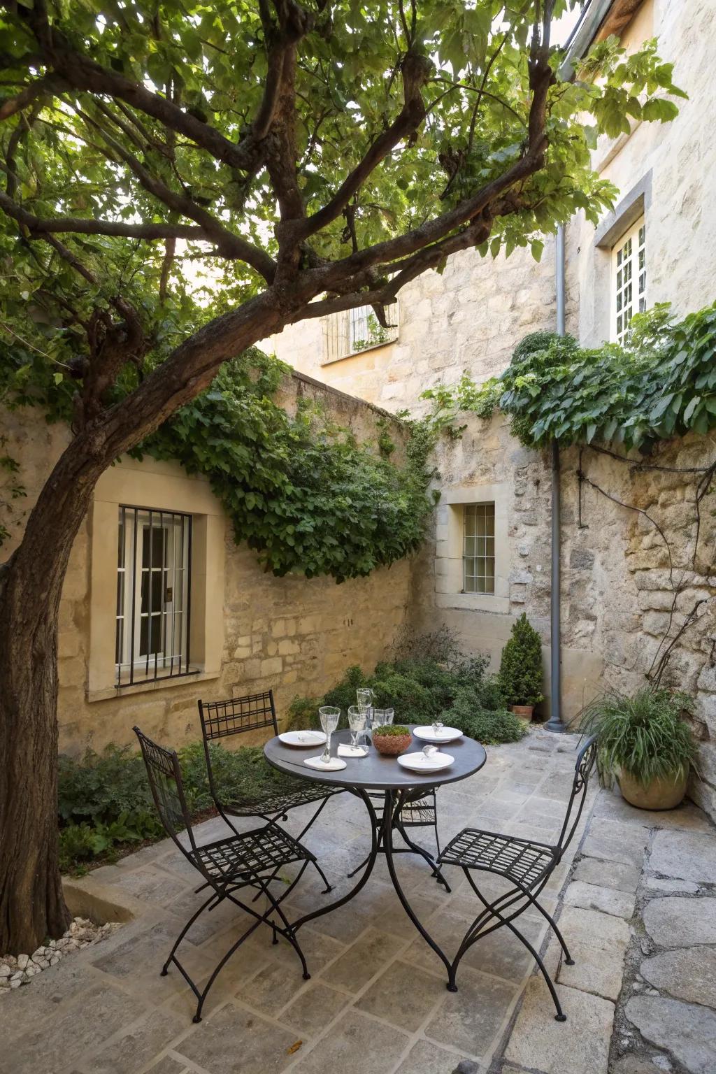 A small courtyard with a wrought iron bistro table and chairs under a tree.