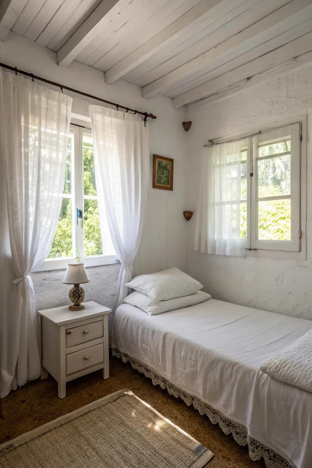 Sheer curtains keep a small white bedroom bright and airy.